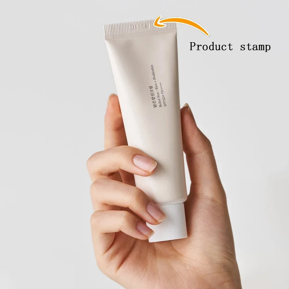 Hand holding a white tube of cream against a light gray background